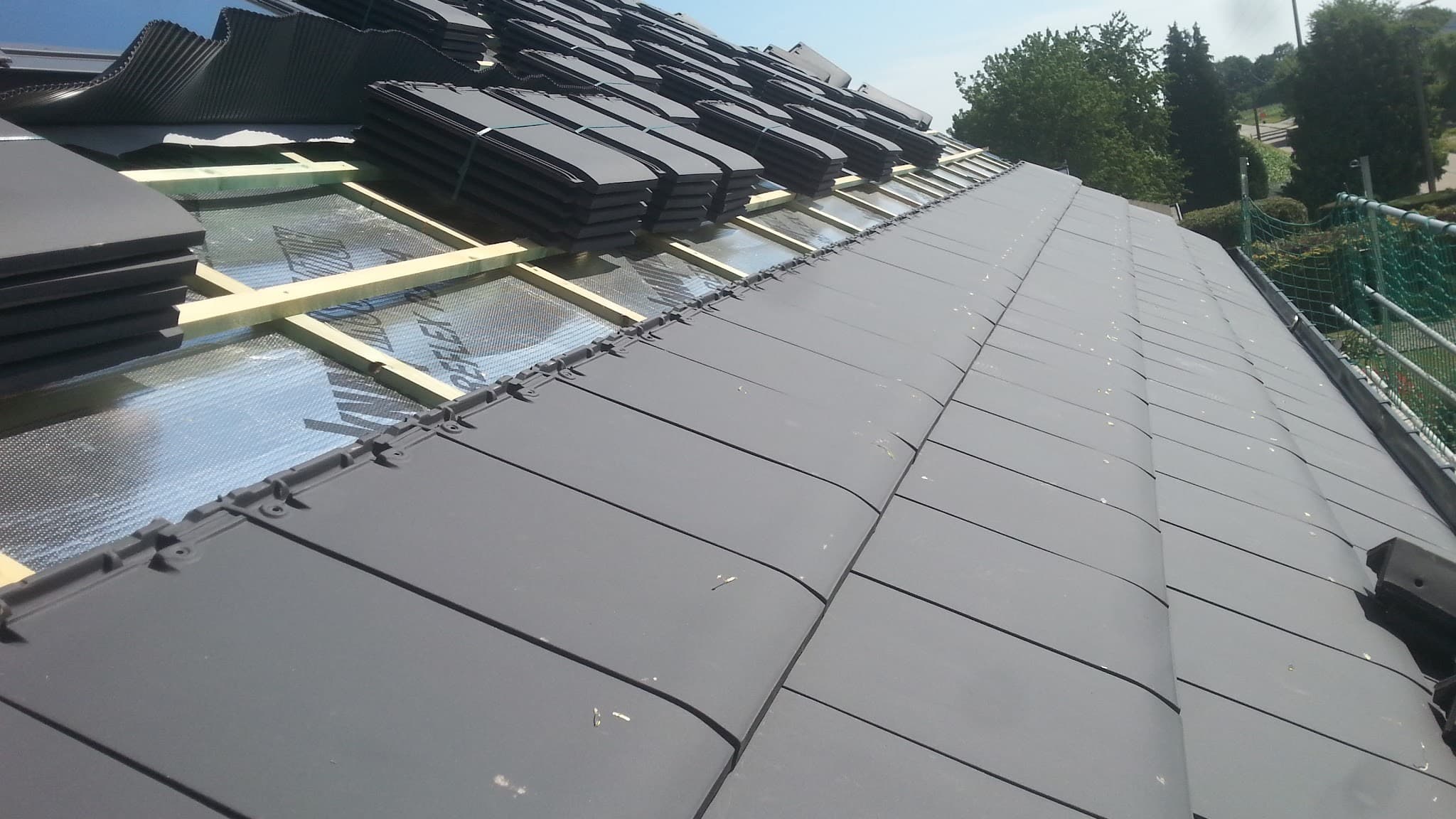 Pose de tuiles anthracite sur une toiture en cours de rénovation par Lazo